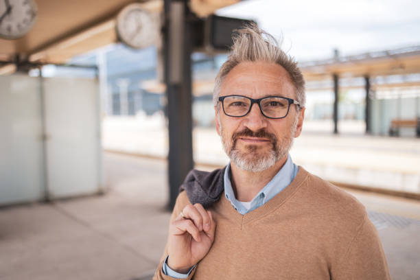 istock Mature man standing confidently at a train station while commuting. He is holding his jacket over his shoulder and looking directly at the camera, embodying a professional and composed appearance. 2181814161