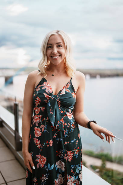 Portrait of a beautiful woman wearing a floral dress and smiling directly at the camera while posing on the rooftop patio of an upscale restaurant where she is having dinner and drinks with friends.