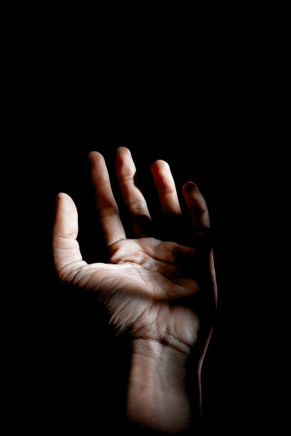 istock Male hand reaching for light in darkness on isolated black background. Selective focus on hand 2181834080