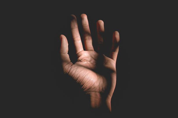 Male hand reaching for light in darkness on isolated black background. Selective focus on hand