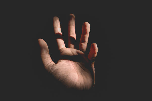 istock Male hand reaching for light in darkness on isolated black background. Selective focus on hand 2181834104