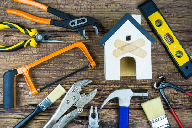 istock The image shows various hand tools arranged around a small house model with two band-aids crossed on its front, all set on a wooden surface. It's a great representation of home repair and maintenance. 2181843290