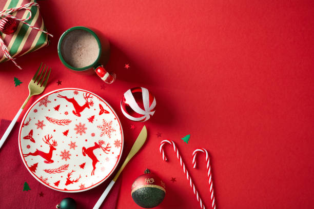 istock Christmas dinner set. Empty plate with deer pattern, vintage decorations, gift box, cup of cacao drink, candy canes on red background. Flat lay, top view. 2181854530