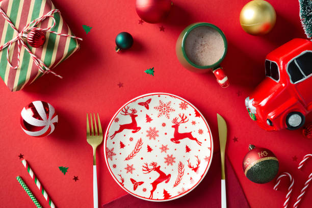 istock Christmas deer pattern dinner plate, gold cutlery, Xmas decorations, vintage gift box, baubles, truck with Christmas tree on red background. New Year table setting.Top view, flat lay. 2181854544