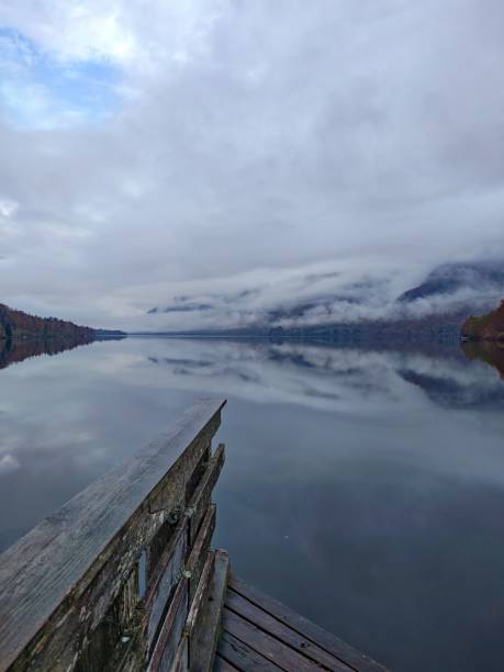 istock Serene lakeside view with wooden dock and misty mountains. 2181855171