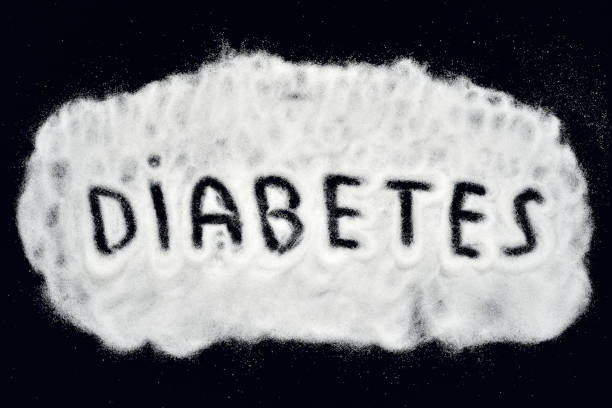 Word DIABETES written on the scattered refined white sugar on the black background. Top view. Stop diabetes and healthy diet concept.
