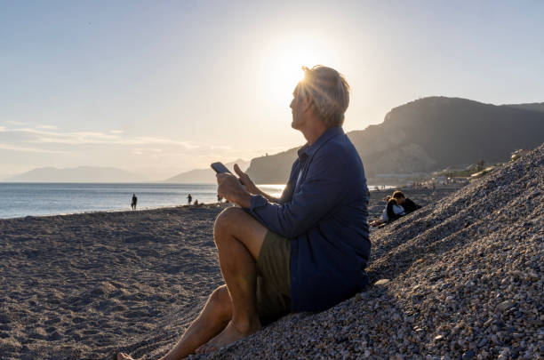 istock Mature man uses mobile phone on beach 2181863755