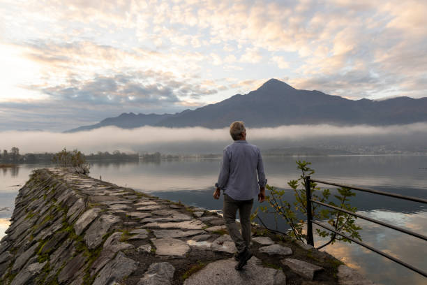Mature man watches sunrise on lakeshore, Lake Como