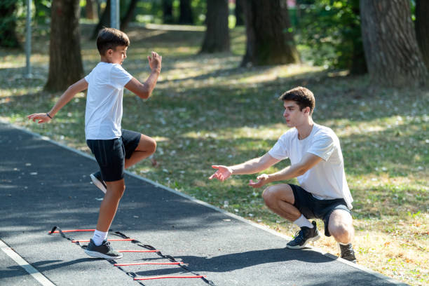 istock Boy exercises outdoors with a trainer using an agility ladder. The session promotes coordination, speed, and physical fitness in a fun, engaging environment under the guidance of a professional. 2181869274