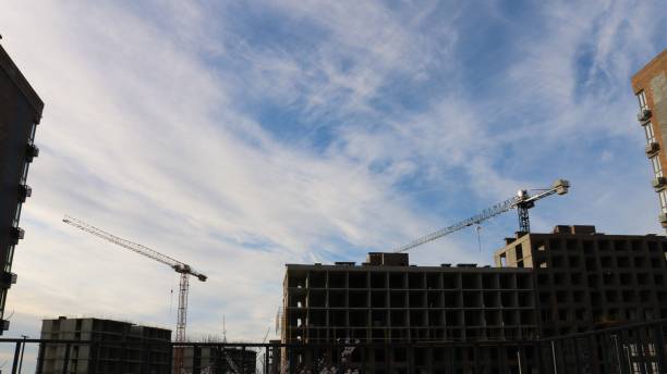istock Two construction cranes stand behind houses against the sky 2181876309