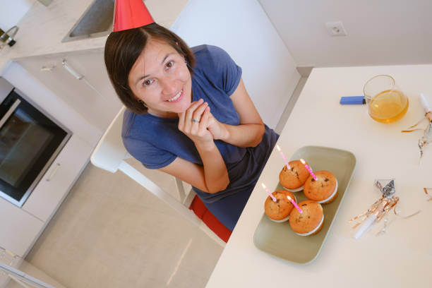 Woman celebrates with four cupcakes topped with candles in place of traditional birthday cake. Smiling and joyful, he enjoys cozy and unique celebration, creating warm and memorable festive moment.