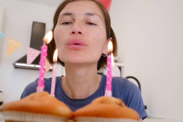 Woman celebrates with four cupcakes topped with candles in place of traditional birthday cake. Smiling and joyful, he enjoys cozy and unique celebration, creating warm and memorable festive moment.