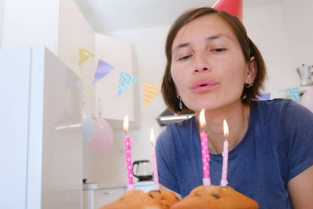 Woman celebrates with four cupcakes topped with candles in place of traditional birthday cake. Smiling and joyful, he enjoys cozy and unique celebration, creating warm and memorable festive moment.