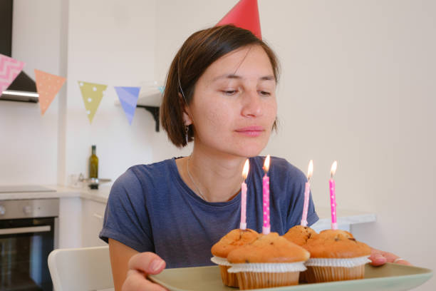 Woman celebrates with four cupcakes topped with candles in place of traditional birthday cake. Smiling and joyful, he enjoys cozy and unique celebration, creating warm and memorable festive moment.