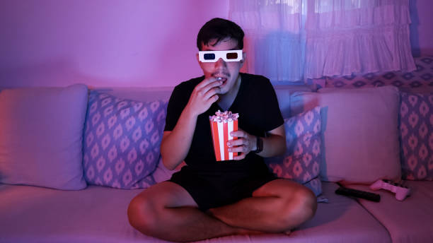 istock Young man eating popcorn while watching a movie at home 2181885427