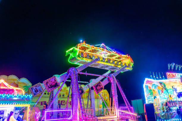 The Frisbee ride on a municipal fair in Schlieren, Switzerland.  The pendulum amusement ride features a circular gondola. It is illuminated in red and violet on the background of dark cloudy sky.
