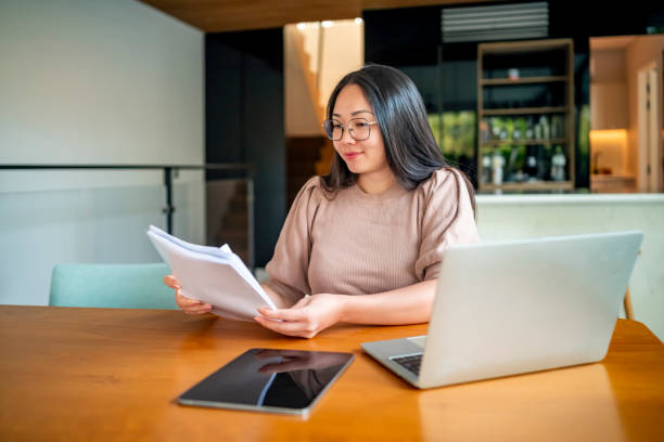 istock Woman Reviewing Documents at Home with a Laptop and Tablet 2181893456