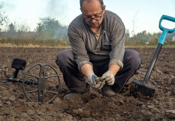 istock A dedicated treasure hunter meticulously digs into the soil, unearthing potential finds. The setting sun casts a warm glow over the empty field, highlighting his focused expression and tools nearby 2181898358