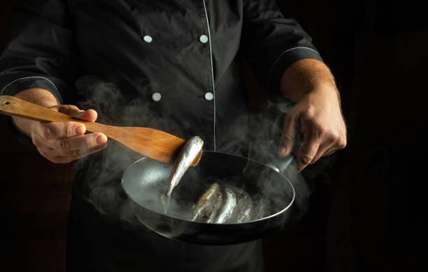 In a dimly lit kitchen, a chef expertly flicks fresh fish into the air, creating a tantalizing steam cloud. The scene captures the art of cooking with passion and precision