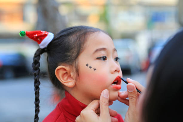 Close up mother applying lipstick over daughter mouth.