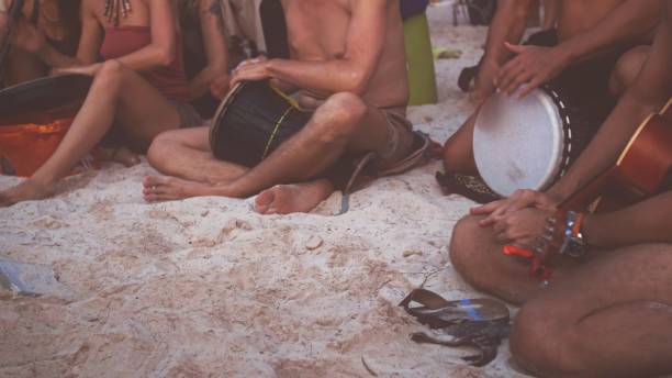 Musicians sit cross legged on white sand beach, creating rhythmic beat on various hand drums. atmosphere radiates joy and togetherness as they enjoy vibrant sounds of summer. beach jam session concept