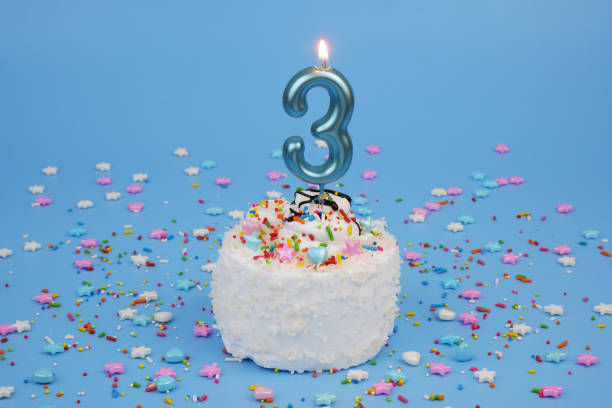 istock Coconut birthday cake on blue background with burning candle, number 3 2181909389