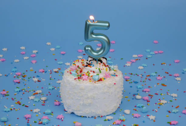 istock Coconut birthday cake on blue background with burning candle, number 5 2181909411