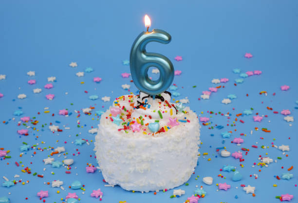 istock Coconut birthday cake on blue background with burning candle, number 6 2181909413