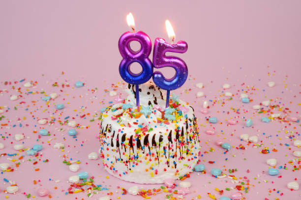 istock Birthday cake with burning candles number 85 on pink background. 2181910079