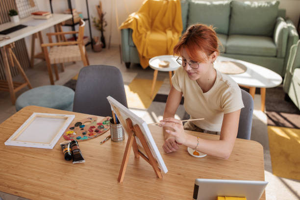 istock Young woman painting at home and using a tablet 2181910715