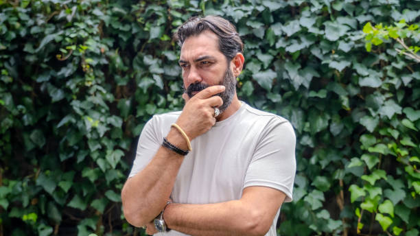 istock A middle-aged, fair-skinned, dark-haired man with a beard is outdoors in a wooded area, looking at the camera in a close-up shot with his hand on his chin, appearing thoughtful 2181931918