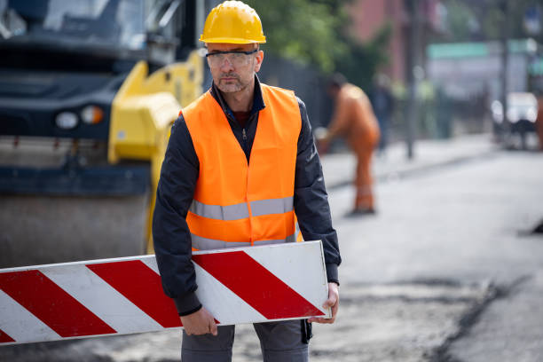 istock Construction worker in reflective safety gear holding a barrier while overseeing road work in a busy urban environment 2181938599