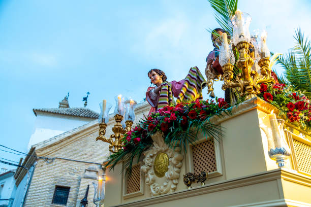 Castro del Rio, Cordoba - Spain - 03-24-2024: Procession figure on a decorated float, adorned with flowers and candle holders, outdoors in a festive atmosphere during a Spanish religious Easter procession.