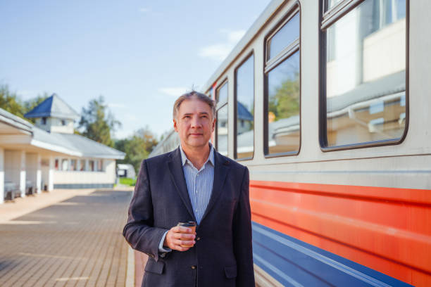 A mature businessman stands on the platform waiting to board a train.
