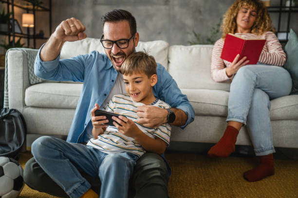 istock dad and son and play video games on cellphone with mum behind 2181945826