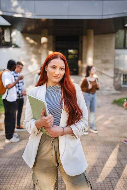 istock Students engaging in outdoor study session on campus while one confidently poses in business attire with a notebook in hand 2181951572