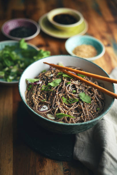 Traditional Korean starch noodles chapche with vegetables and beef in a white round plate on a gray background, chopsticks lay on a plate with noodles. side view.