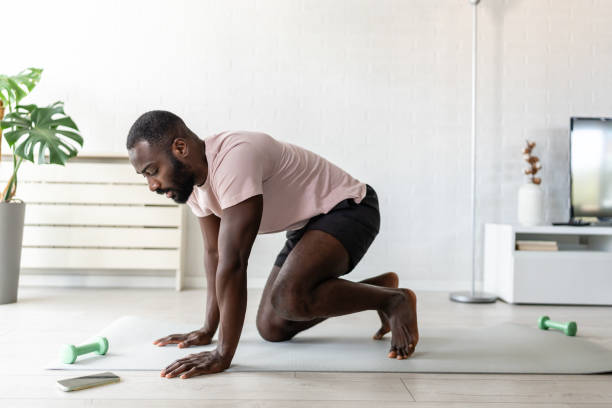 istock Young African-American man practicing yoga on a mat at home, focused on a strength and flexibility exercise in a bright, modern living room with indoor plants 2181961499