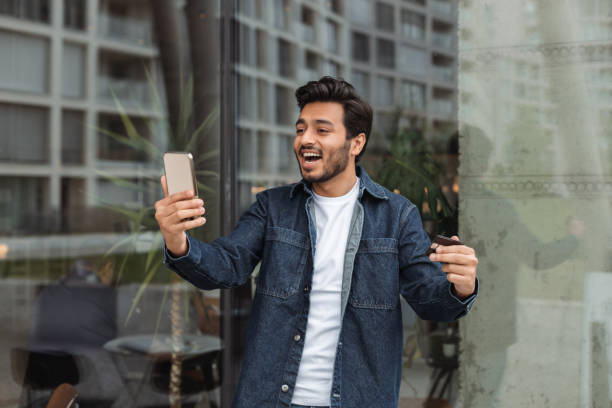istock Excited man making online payment using smartphone and credit card outside cafe 2181963797