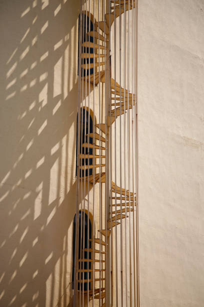 Spiral staircase mounted outside the building droppping shadows on a wall. Vertical shot, modern architecture concept