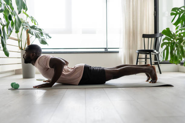 istock Young African-American man doing yoga on a mat in a bright home setting, practicing the cobra pose with focused posture. Surrounded by plants, promoting wellness and relaxation. 2181967506