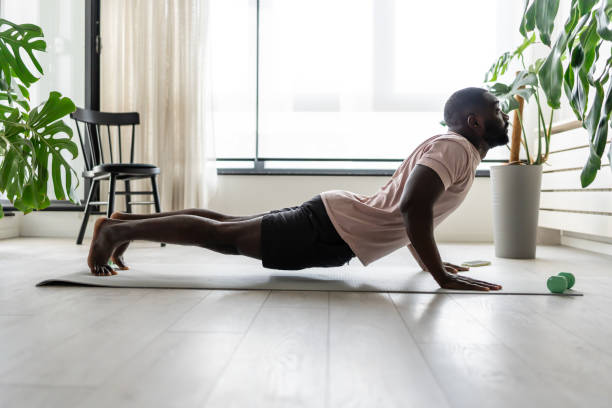 istock Young African-American man doing yoga on a mat in a bright home setting, practicing the cobra pose with focused posture. Surrounded by plants, promoting wellness and relaxation. 2181967545