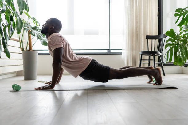 istock Young African-American man doing yoga on a mat in a bright home setting, practicing the cobra pose with focused posture. Surrounded by plants, promoting wellness and relaxation. 2181967645