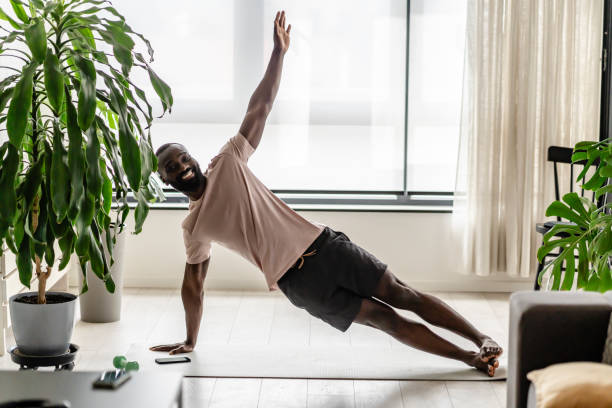 istock Young African-American man doing a side plank exercise on a yoga mat at home, practicing strength and balance in a bright living room with indoor plants 2181969033