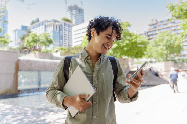 istock Smiling young man using smartphone outdoors holding laptop 2181975412
