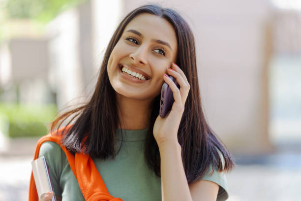 Happy student talking on the phone while walking outdoors