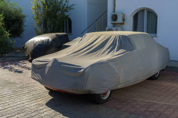 istock Classic cars covered with dust covers under bright sunlight in a peaceful driveway setting 2181980119