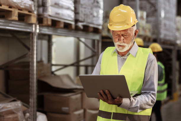 istock Senior Male Supervisor Working on Laptop at Distribution Warehouse 2181982732