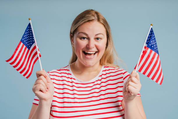 istock Smiling young plus size woman holding American flags posing isolated on blue background 2181983585