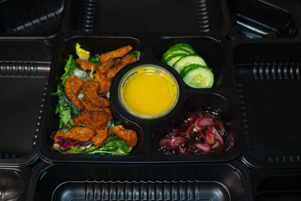istock A salad in a black plastic container surrounded by catering containers, featuring fresh greens, vegetables, and sauce. 2181988011